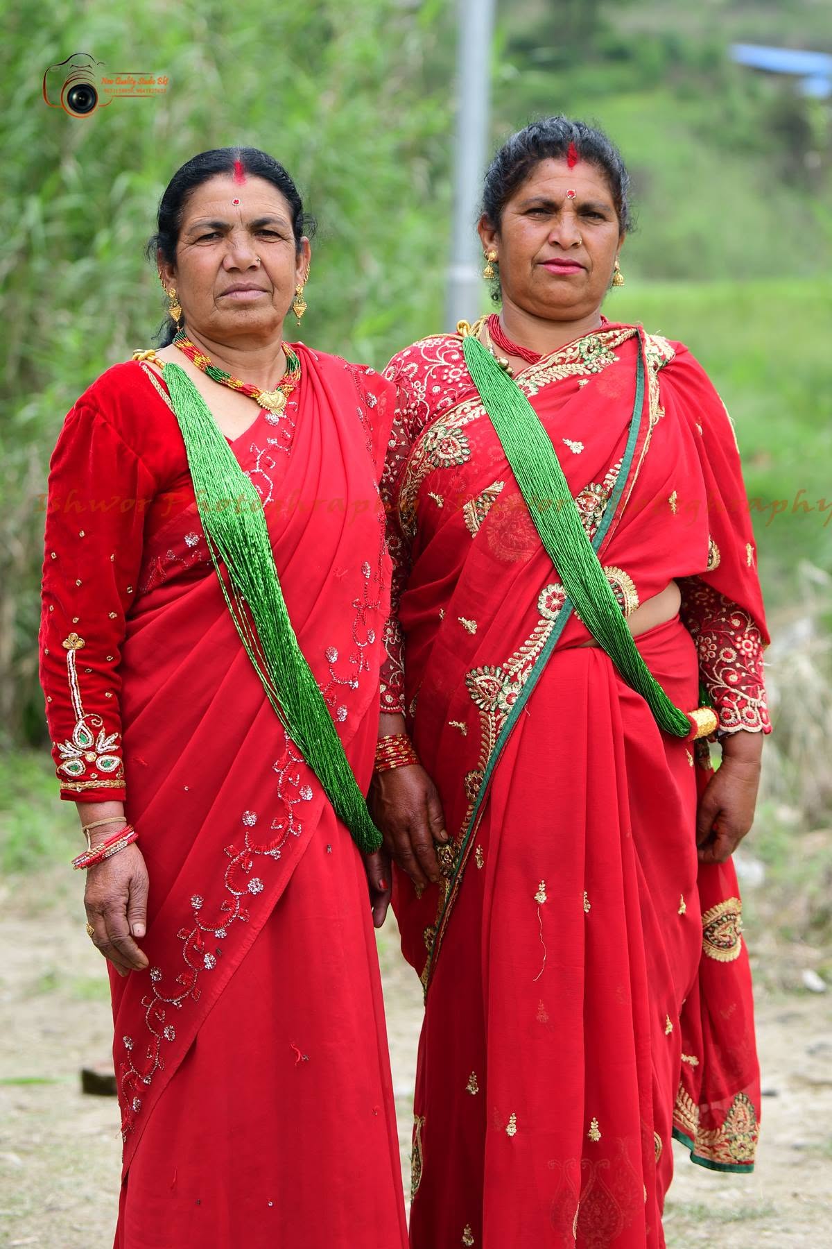 Two women in red saris photographed outdoors at a ceremony
